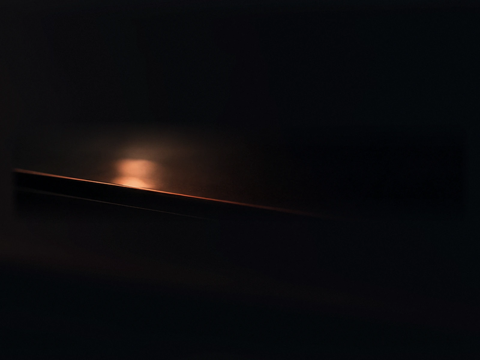 A dark surface at night catching a single warm reflection, as if a decision is being made out of frame.